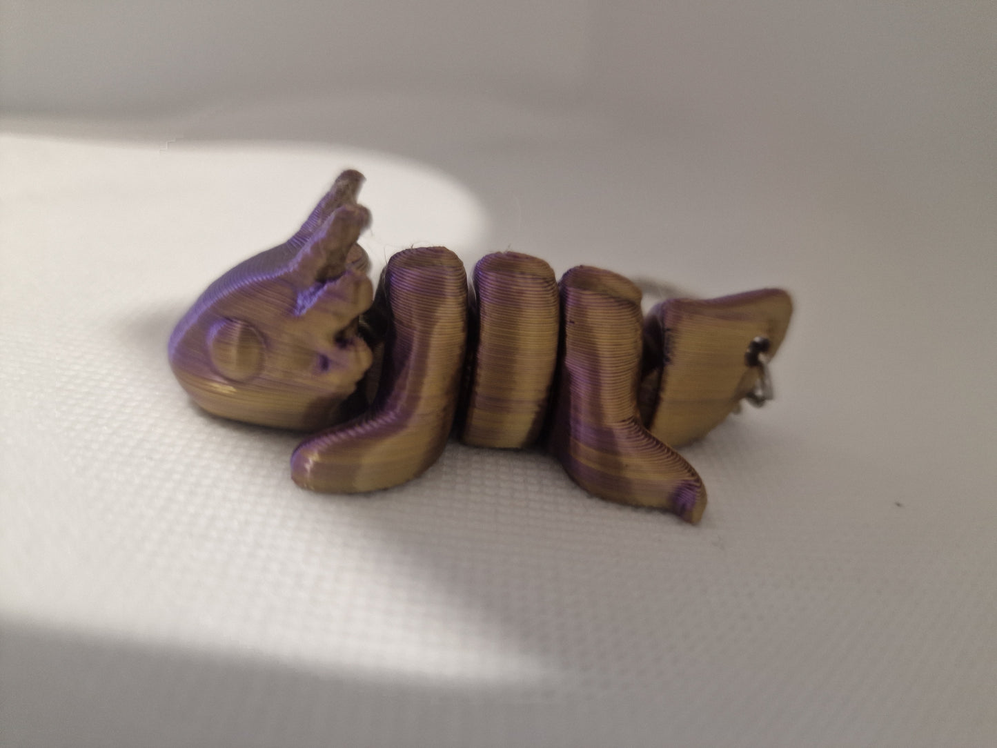 A charming 3D-printed fox keyring with an articulated body, designed in vibrant purple and gold tones. The compact size (7cm x 3cm x 2.5cm) makes it ideal for keys or bags, blending practicality with a playful, handmade touch