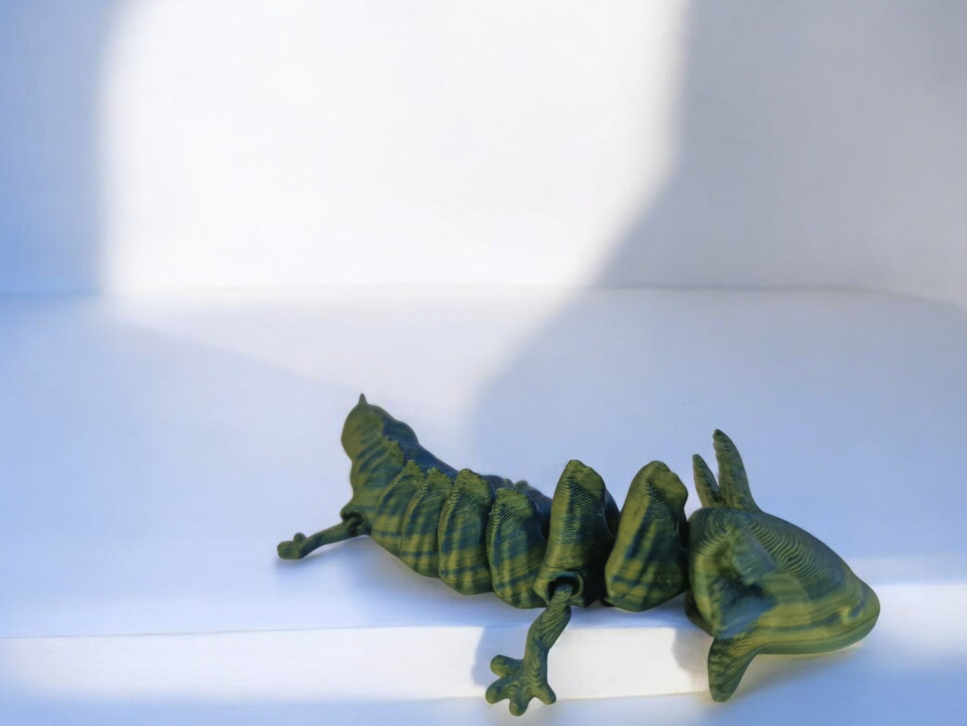 A vibrant 3D-printed axolotl figurine, 6 inches long, with fully articulated limbs, tail, and head for endless posing options. Designed in a stunning two-tone mix of blue, green, and yellow, the piece is lightweight, durable, and perfect for display on desks or shelves. A unique and eye-catching addition for collectors or axolotl enthusiasts.