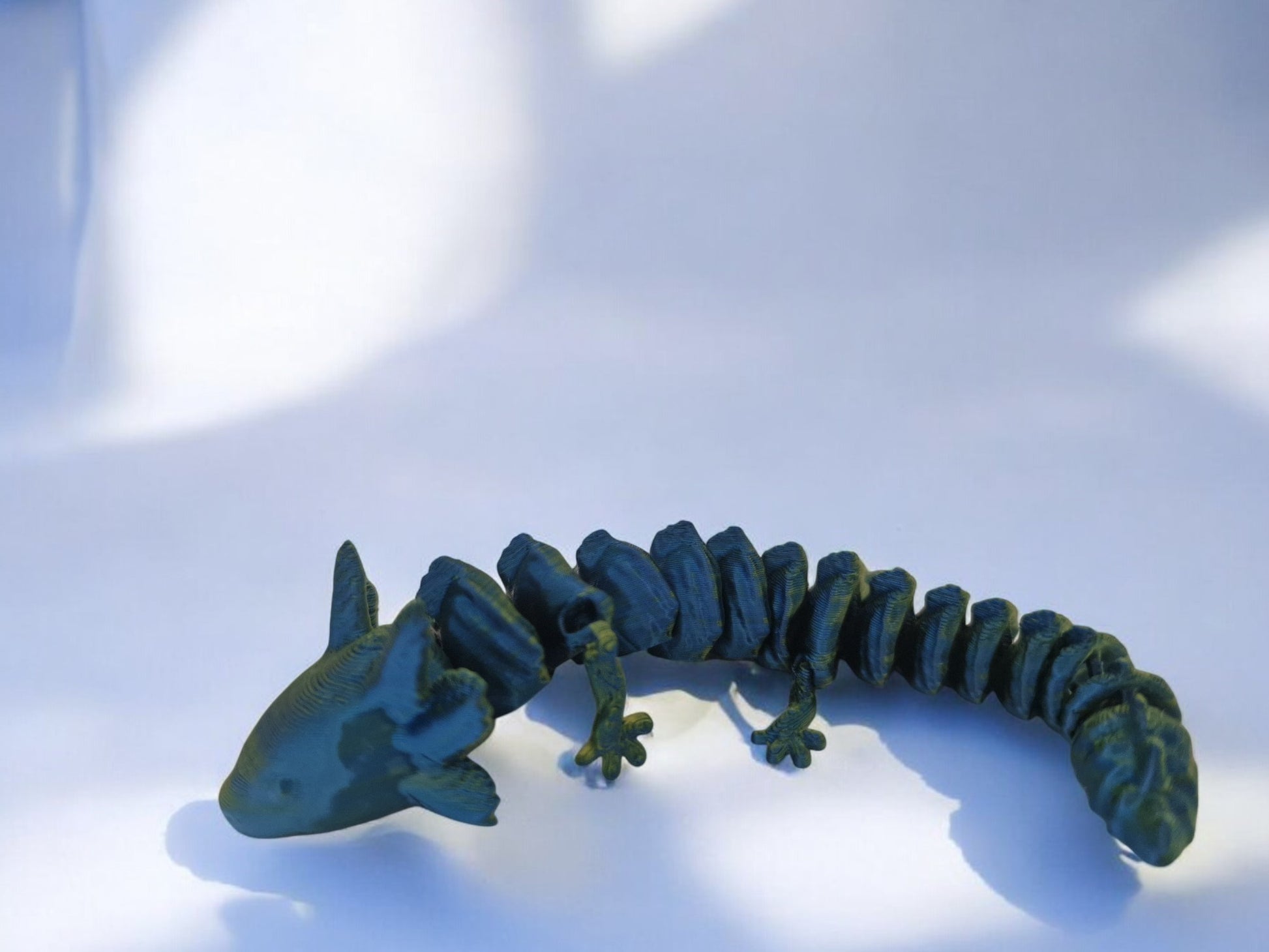 A vibrant 3D-printed axolotl figurine, 6 inches long, with fully articulated limbs, tail, and head for endless posing options. Designed in a stunning two-tone mix of blue, green, and yellow, the piece is lightweight, durable, and perfect for display on desks or shelves. A unique and eye-catching addition for collectors or axolotl enthusiasts.