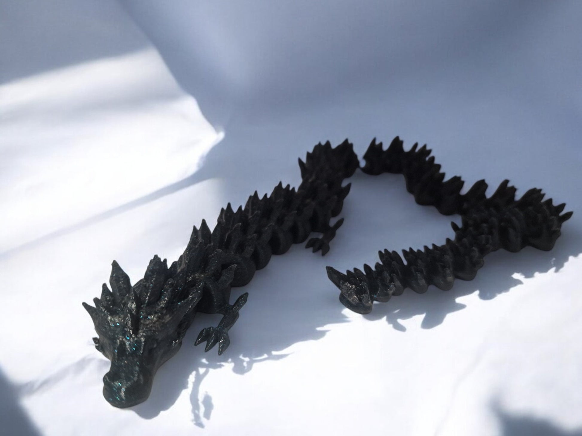 A stunning black 3D-printed dragon figurine adorned with shimmering blue speckles, measuring approximately 35cm. Featuring intricate details such as textured scales, majestic wings, and a fierce expression, this durable and unique display piece is perfect for fantasy lovers, collectors, and mythical decor enthusiasts.
