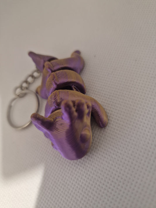 A charming 3D-printed fox keyring with an articulated body, designed in vibrant purple and gold tones. The compact size (7cm x 3cm x 2.5cm) makes it ideal for keys or bags, blending practicality with a playful, handmade touch