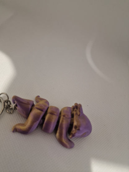 A charming 3D-printed fox keyring with an articulated body, designed in vibrant purple and gold tones. The compact size (7cm x 3cm x 2.5cm) makes it ideal for keys or bags, blending practicality with a playful, handmade touch