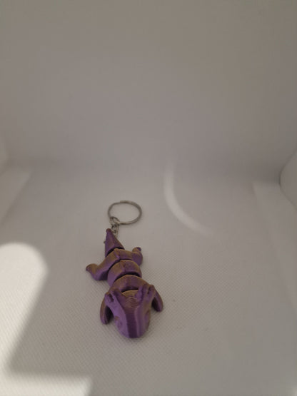 A charming 3D-printed fox keyring with an articulated body, designed in vibrant purple and gold tones. The compact size (7cm x 3cm x 2.5cm) makes it ideal for keys or bags, blending practicality with a playful, handmade touch