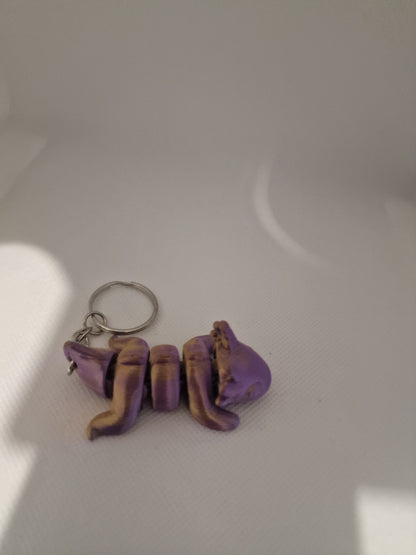 A charming 3D-printed fox keyring with an articulated body, designed in vibrant purple and gold tones. The compact size (7cm x 3cm x 2.5cm) makes it ideal for keys or bags, blending practicality with a playful, handmade touch