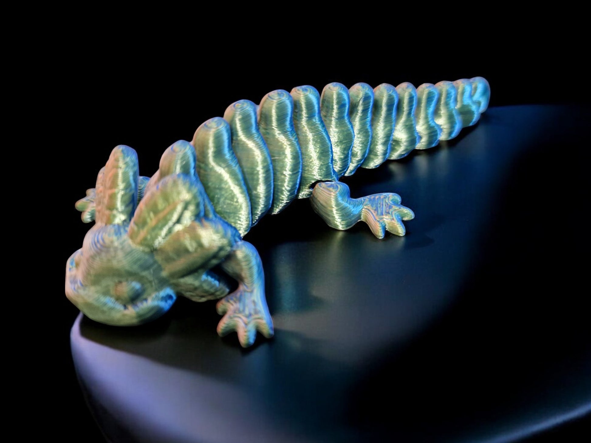 A 3D-printed articulating axolotl figurine with movable limbs and tail, measuring 9cm long, 4cm wide, and 3cm high. This durable, lightweight piece features a random dual-tone color design, making it a playful and unique display item or gift for axolotl enthusiasts and collectors.