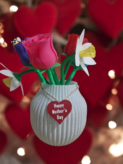 flower pot with red silk rose, two additional roses, two daffodils, love heart pendants reading 'I Love You' and 'Happy Mother’s Day', and a cute bee. Dimensions: 28cm (H) x 18cm (W) x 18cm (D). Perfect for Mother’s Day or Valentine’s Day, a lasting gift that doesn’t wilt.