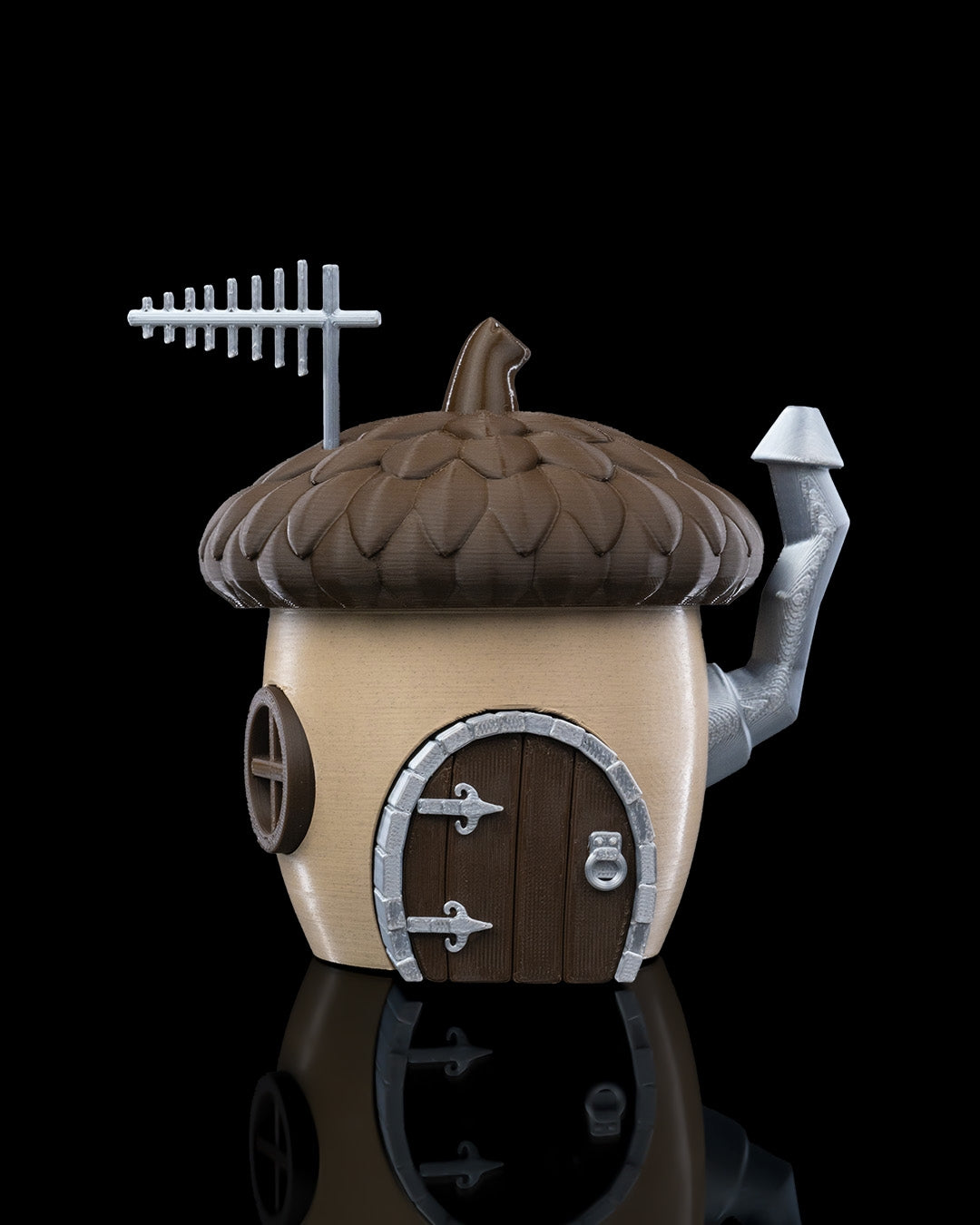 A charming acorn-shaped house decoration featuring a textured brown roof, circular window, wooden door with silver accents, and a chimney. Perfect for gardens, small pet enclosures, or reptile terrariums, set against a natural backdrop of green plants