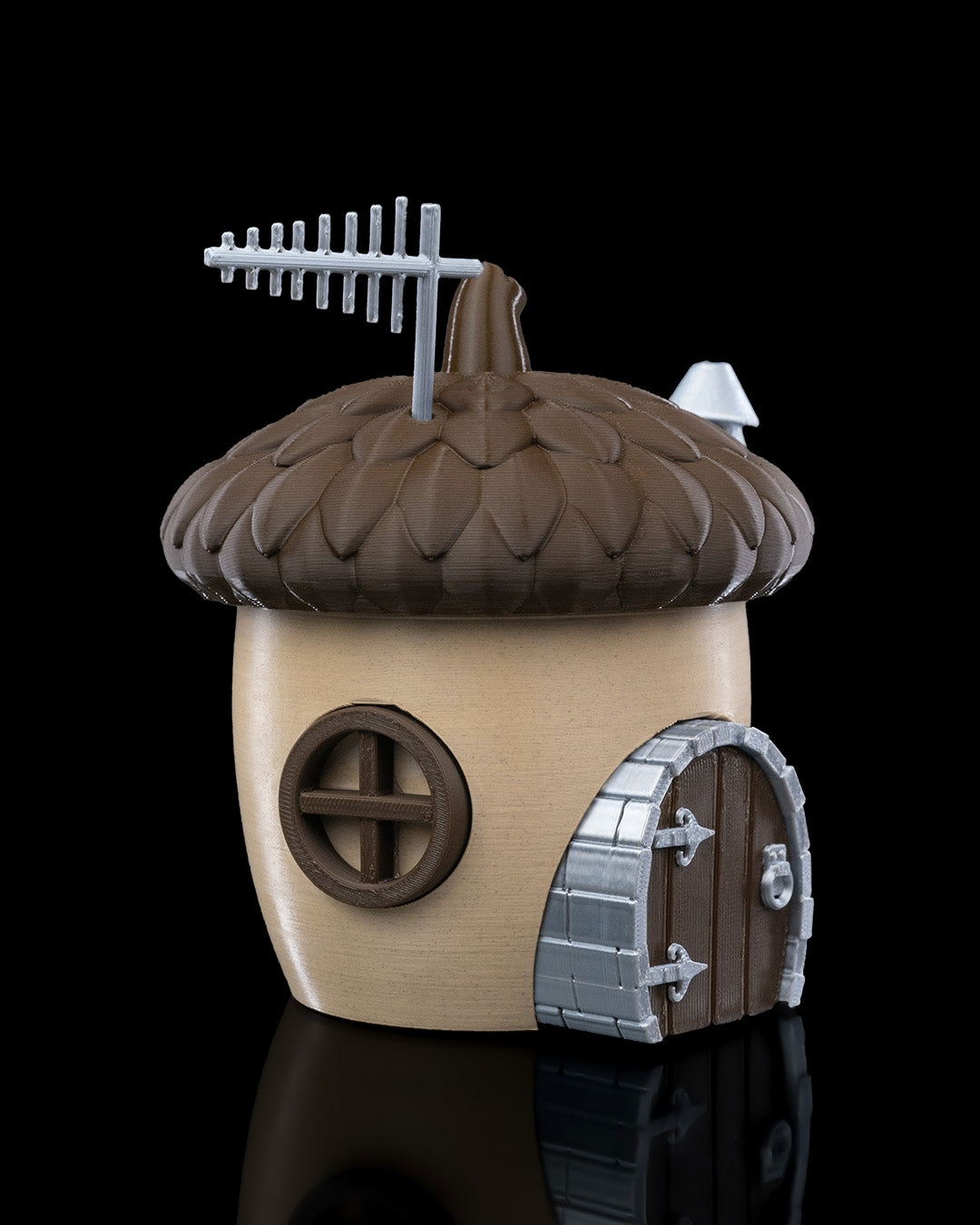 A charming acorn-shaped house decoration featuring a textured brown roof, circular window, wooden door with silver accents, and a chimney. Perfect for gardens, small pet enclosures, or reptile terrariums, set against a natural backdrop of green plants