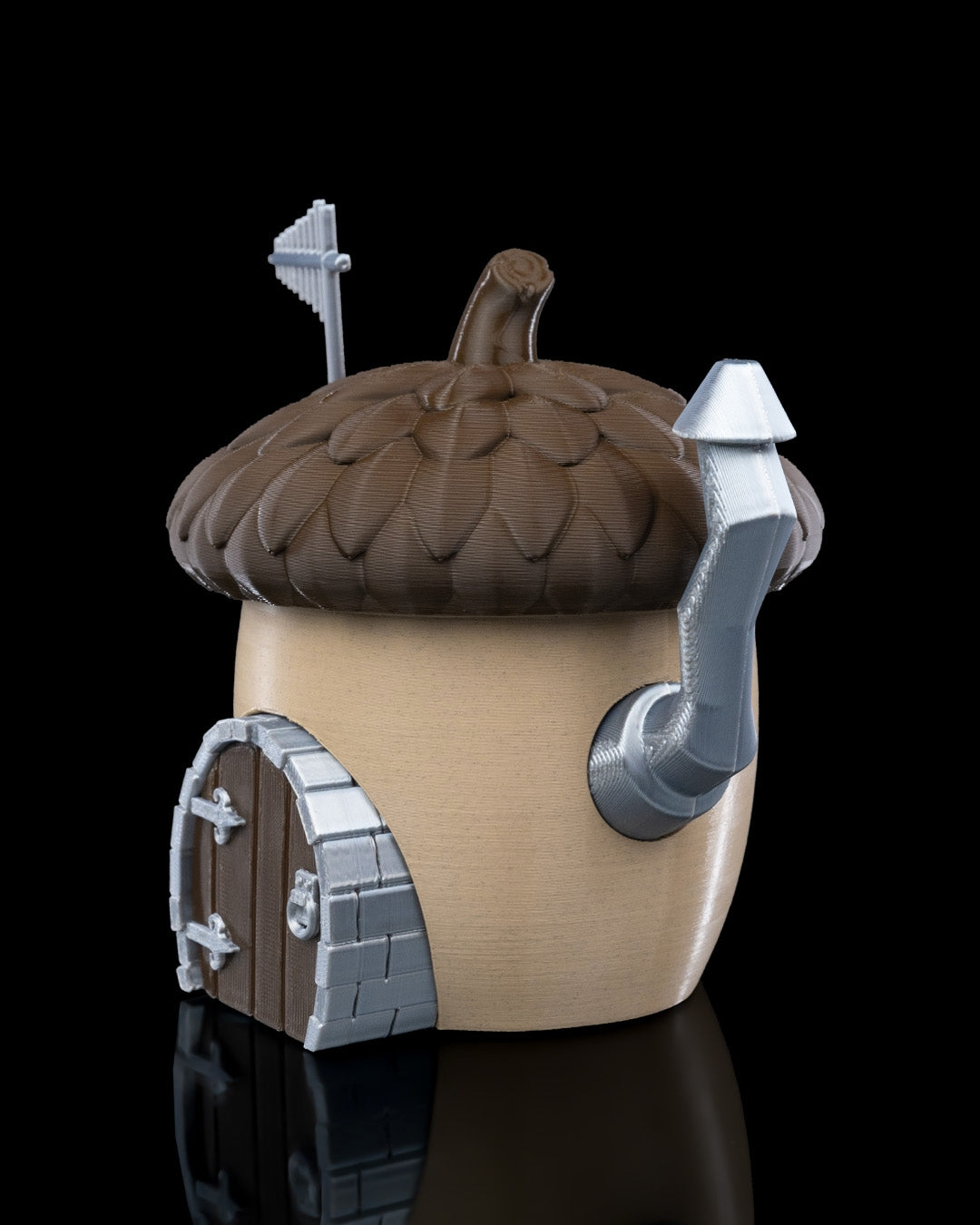 A charming acorn-shaped house decoration featuring a textured brown roof, circular window, wooden door with silver accents, and a chimney. Perfect for gardens, small pet enclosures, or reptile terrariums, set against a natural backdrop of green plants